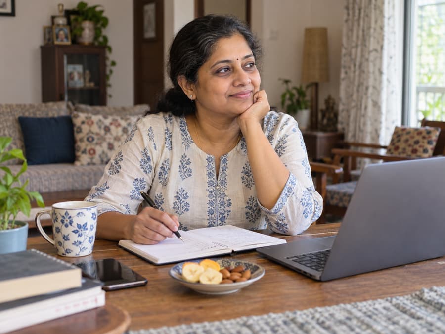 South Indian woman using a notebook beside her laptop in a calm home setting